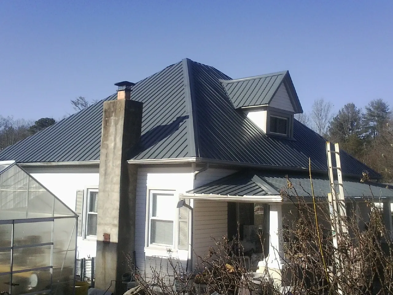 Dark blue standing seam metal roof on a white farmhouse with dormer — Slate & Tile Roof Repair by Roofing Brothers in Palm Desert