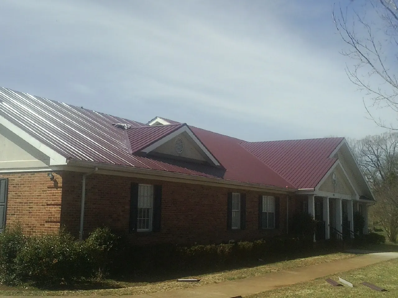 Red metal roof with gabled entries on a long brick building, from a Hail Damage Roof Repair job in Palm Desert