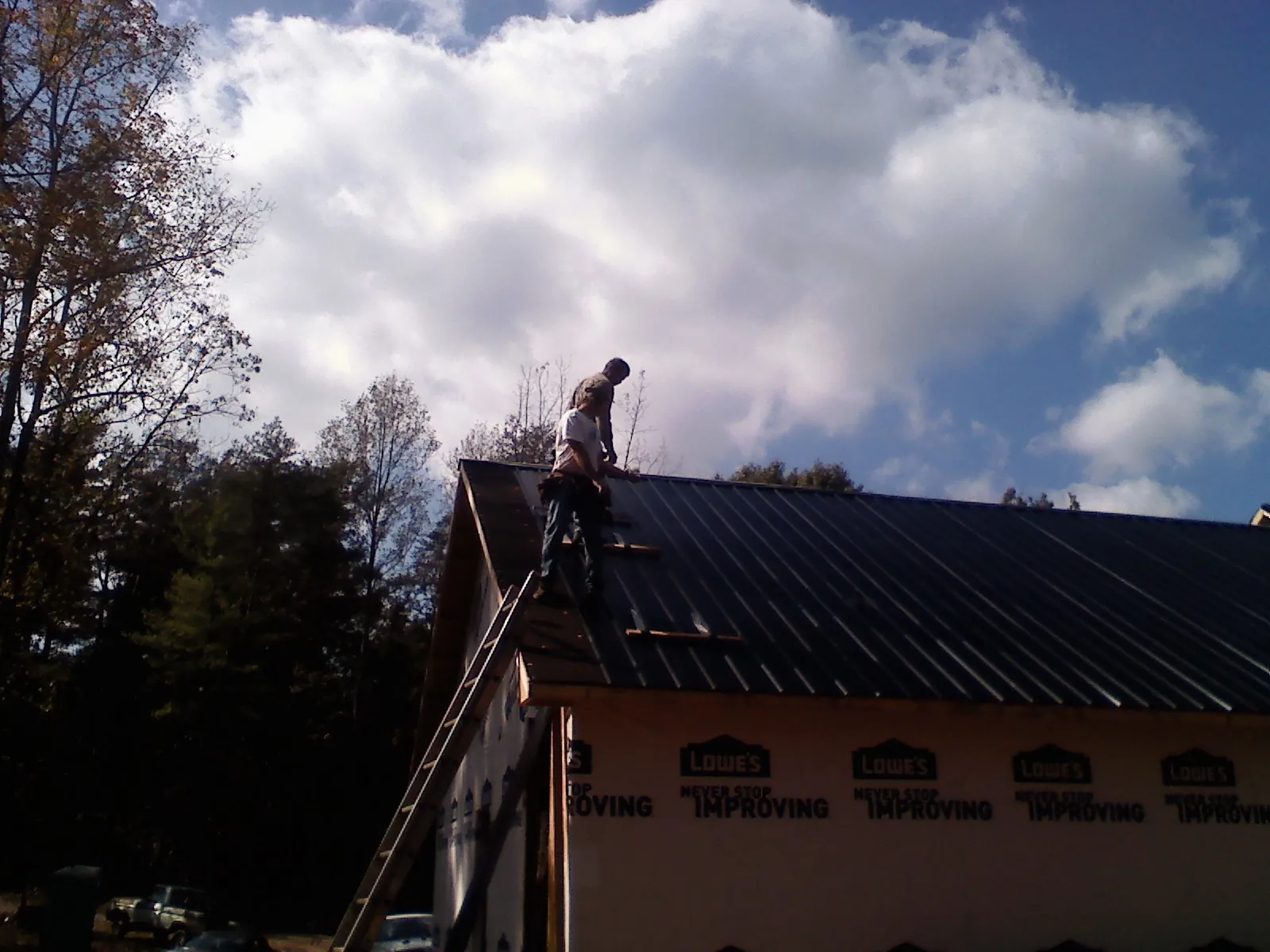 Roofer fastening dark metal panels high against a cloudy sky, from a Roof Inspection job in Palm Desert