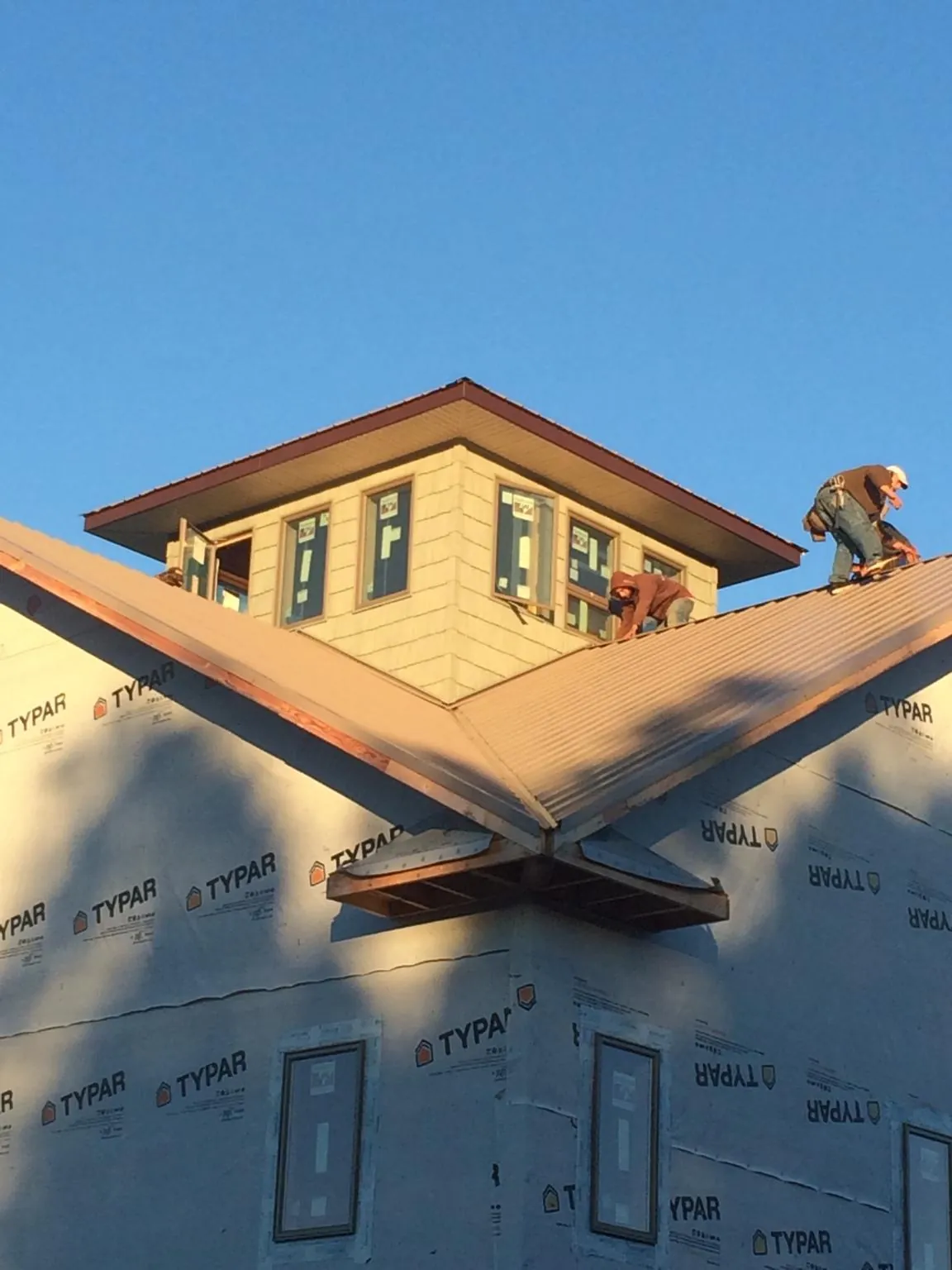 Roofers working around a rooftop cupola on a new metal roof at sunset — Roof Waterproofing in Palm Desert by Roofing Brothers